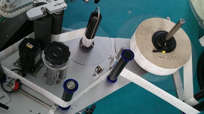 Poltsa eta botila ovalak. Etiketa eranskailuen aplikatzailea. Etiketa autoadhesiboak inprimatzeko makina garraiatzaile luzearekin